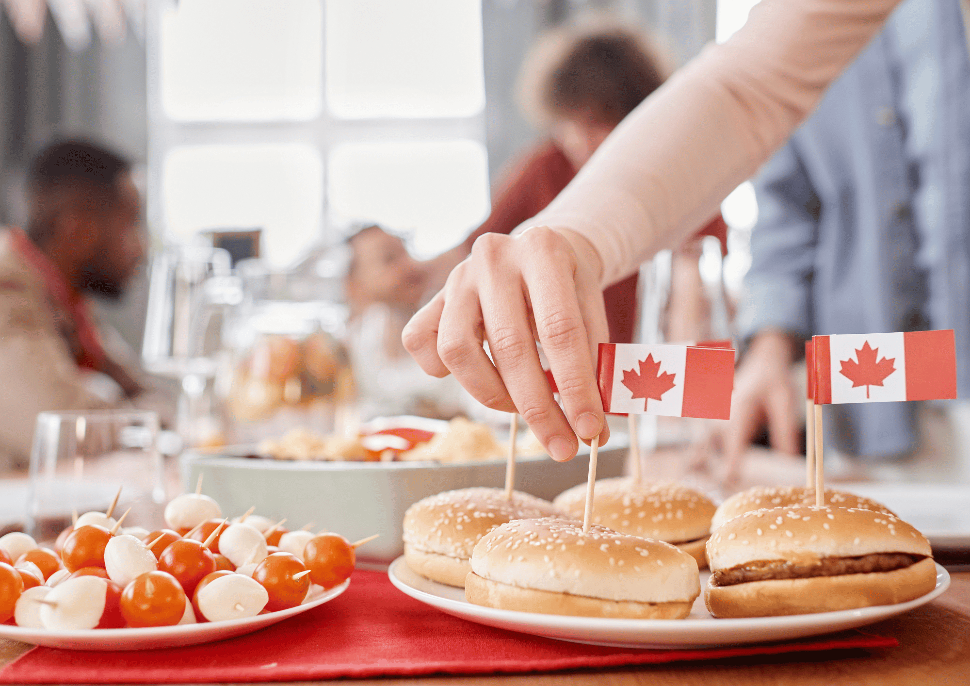 Canada Day Gift Baskets: A hand placing a tiny Canadian flag toothpick into sliders on a party table with appetizers.