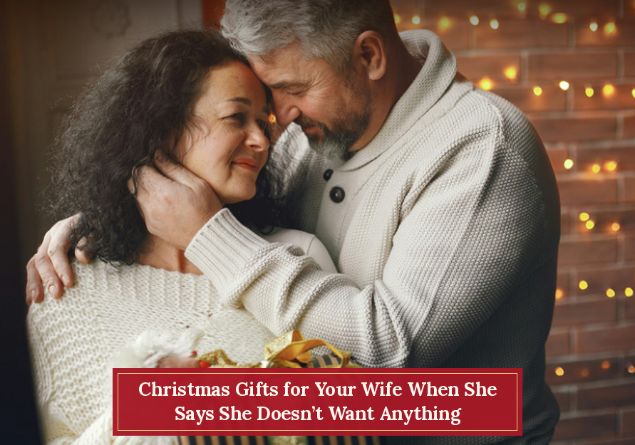 Couple embracing warmly by holiday lights with text "Christmas Gifts for Your Wife When She Says She Doesn't Want Anything".