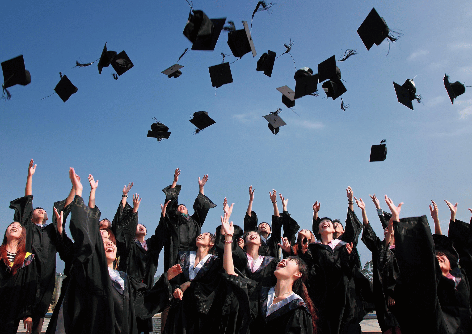 June Graduation Season: A large group of excited graduates throwing their caps into the blue sky during convocation.