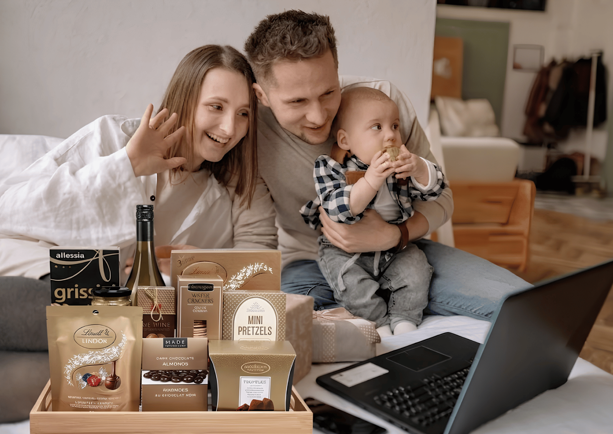 How to Send a Housewarming Gift: A family on a video call next to a gourmet gift basket on a bed.
