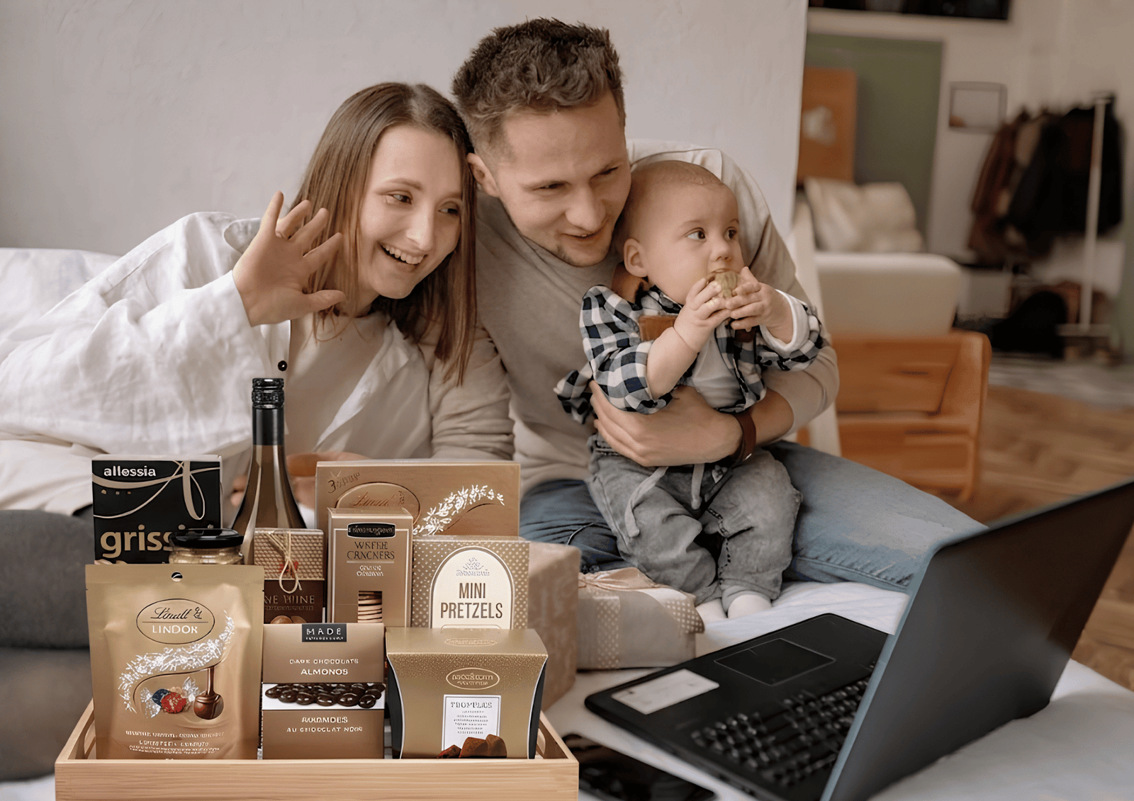 How to Send a Housewarming Gift: A family on a video call next to a gourmet gift basket on a bed.