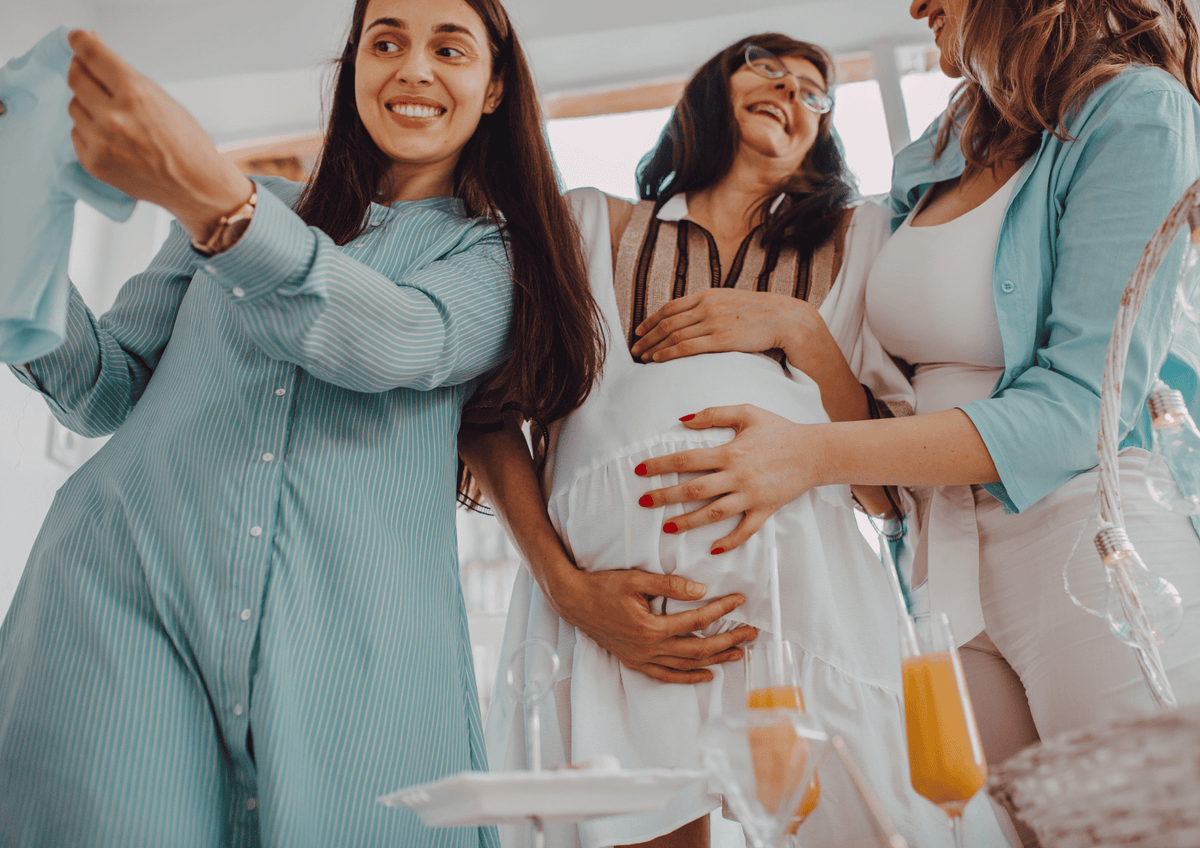 Office Baby Shower Gift Ideas: Coworkers smiling around a pregnant colleague at a party with drinks and baby clothes.