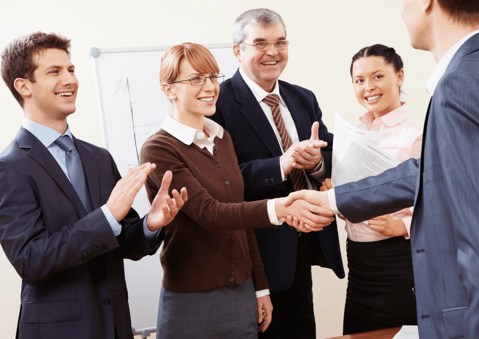 A group of smiling professionals applauding as two colleagues shake hands in an office.