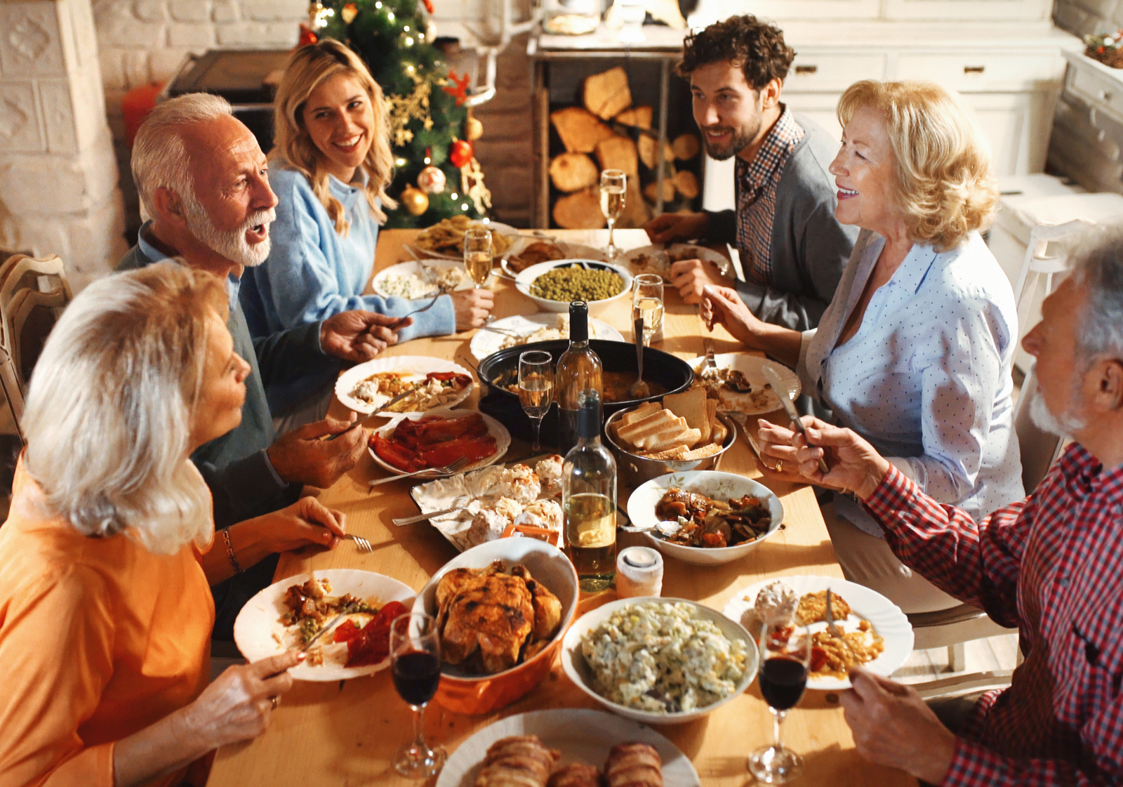 Multi-generational family gathered around a dining table enjoying Christmas dinner together near the tree.