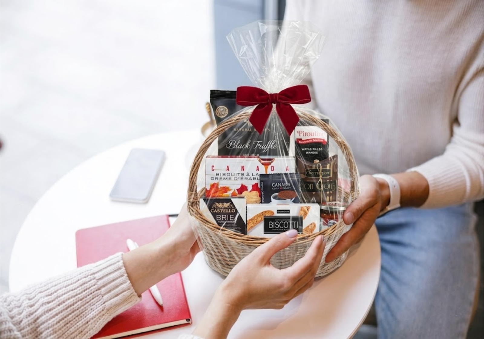 Handing over a Canadian gourmet gift basket wrapped in clear cellophane and topped with a festive red ribbon.