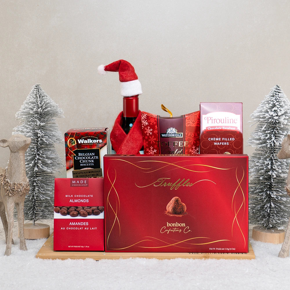 A Spark of Christmas gift basket with red wine in a Santa hat, cocoa truffles, Walkers biscuits and Pirouline wafers