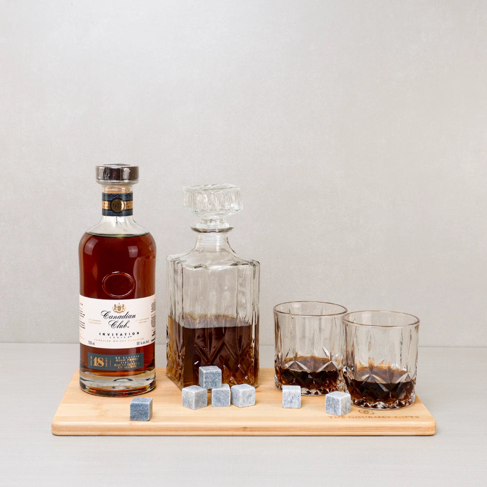 Canadian alcohol gift set with premium whiskey, a decanter, and two glasses on a charcuterie board.