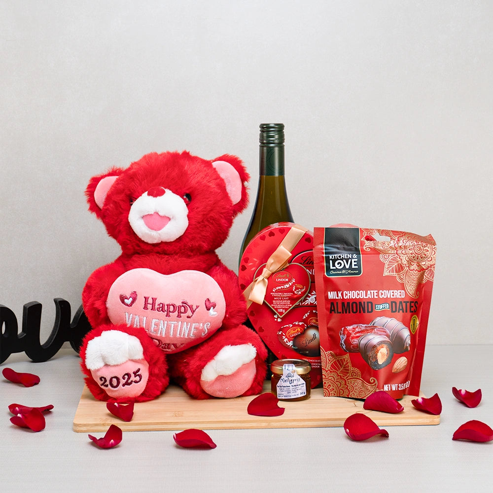 Happy Valentine’s Day Gift Basket with a red teddy bear, white wine, a Lindt Lindor heart box and chocolate-covered dates