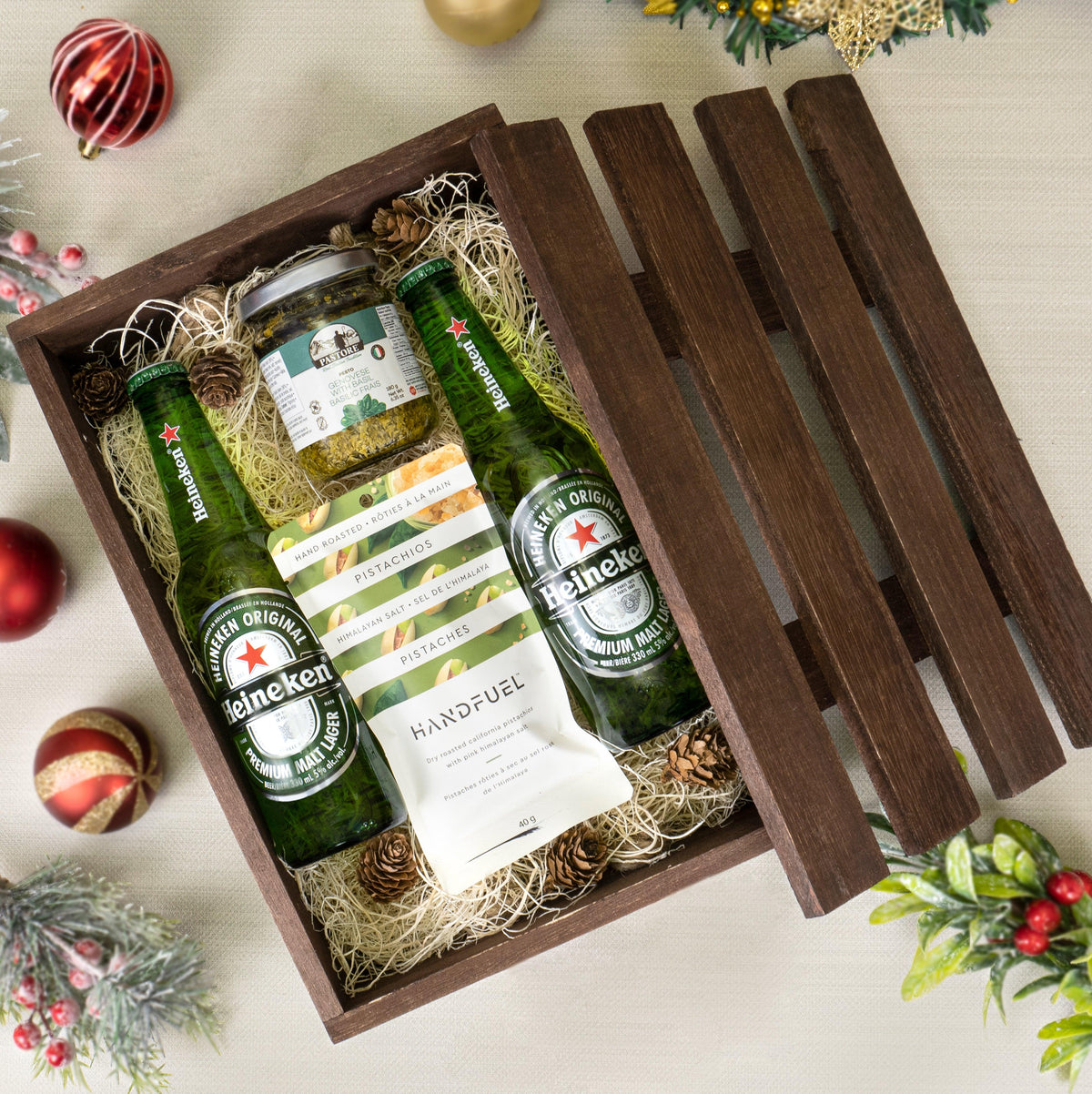 Holiday Cheers Beer & Snacks Basket with two Heineken bottles, basil pesto and Handfuel pistachios in a dark wooden crate
